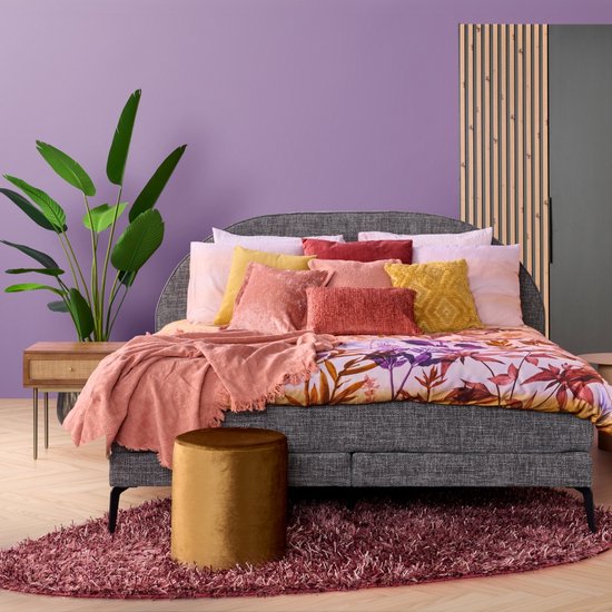 Zachtroze plaid met franjes op een bed met een kleurrijk bloemen dekbed.