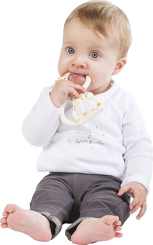 Baby zit op de grond en bijt op een witte Sophie de Giraf bijtring met bruine stippen.