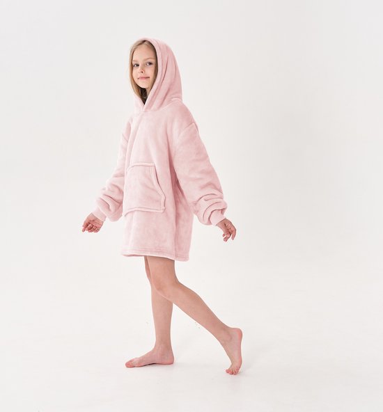 Een jong meisje loopt naar rechts, gekleed in een roze, oversized hoodie met capuchon.