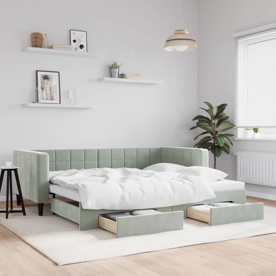 Lichtgrijs fluwelen slaapbank in een woonkamer, met beddengoed en twee open lades onder het bed.