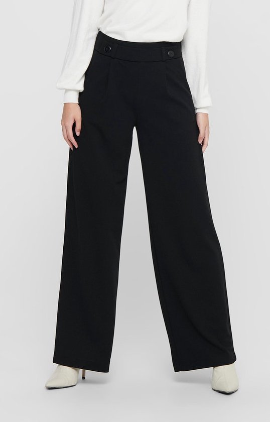 Model met zwarte wijde broek, met knoopdetail, gedragen met witte top.