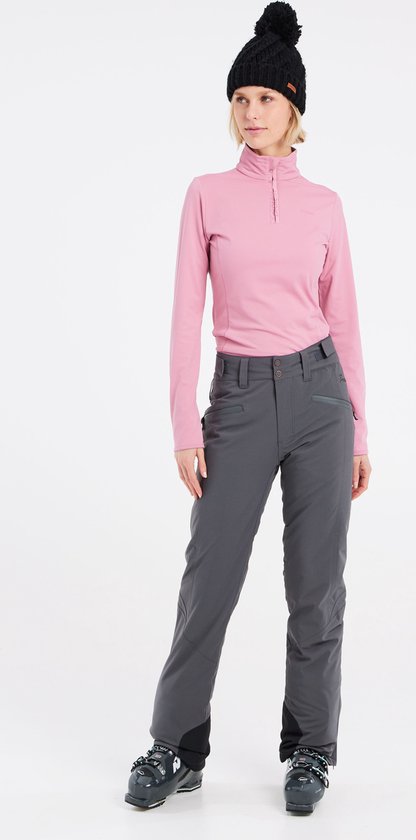 Femme portant un col roulé rose et un pantalon de ski gris, vue de face avec des chaussures de ski.