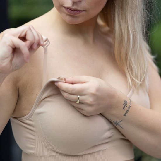 Model toont het openen van de voedingsclip van een beige naadloze bh.