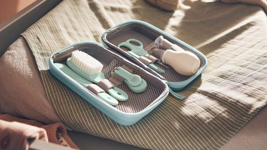 Mintgroene babyverzorgingsset, open in een reishoes, met borstel, kam, schaar en nagelknipper.