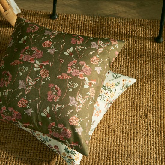 Twee groene sierkussens met een bloemenprint, gestapeld op een bruine jute mat.