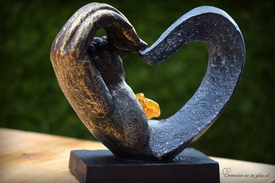 Zwarte hartvormige urn met gouden handen, met een amberkleurige glazen ster.