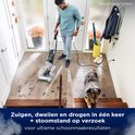 Een man gebruikt de BISSELL HydroSteam stofzuiger met stoom in een gang, met een hond die toekijkt.