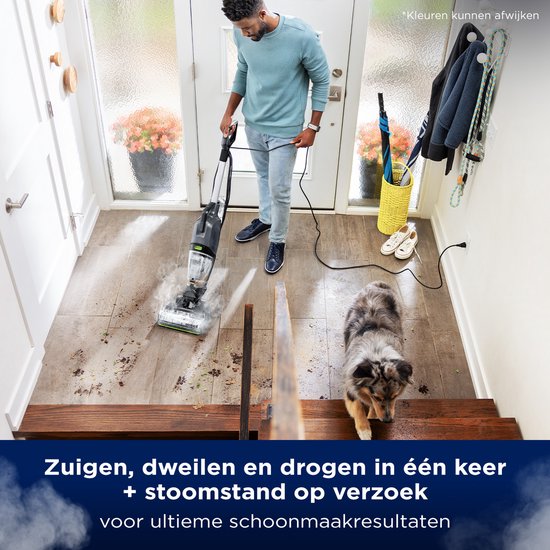 Een man gebruikt de BISSELL HydroSteam stofzuiger met stoom in een gang, met een hond die toekijkt.