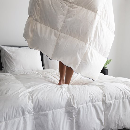 Vrouw met gestreepte pyjama staat op een bed, met een witte donsdeken eroverheen