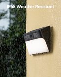 Zwarte camera met witte lamp, bedekt met regendruppels aan een gele muur.