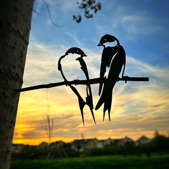 Décoration métallique noire de deux hirondelles sur une branche, sur fond de coucher de soleil.