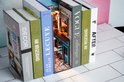 Boekensteun in de vorm van een miniatuur café, tussen gestileerde boeken met titels als 'VOGUE' en 'LECUYE'.