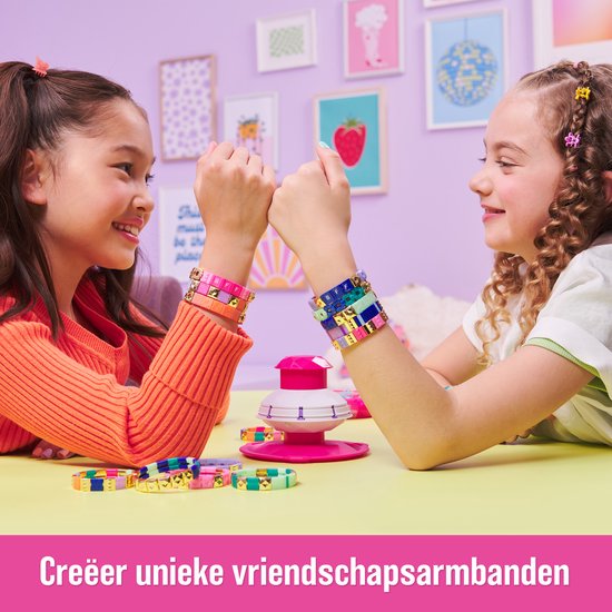 Twee meisjes tonen hun zelfgemaakte armbandjes, de één oranje met roze, de ander blauw met geel.