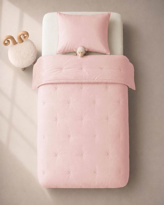 Roze dekbed met kruissteken en een kussensloop op een kinderbed. Een schaapknuffel ligt op het kussen.