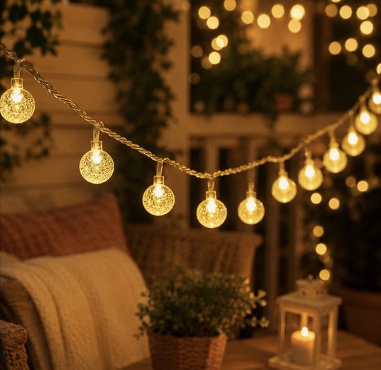 Une guirlande lumineuse de 50 ampoules rondes d'ambiance avec effet filament, suspendue dans un jardin avec un éclairage de fond doux.