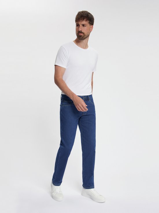 Man met witte t-shirt en donkerblauwe spijkerbroek, looprichting naar voren.