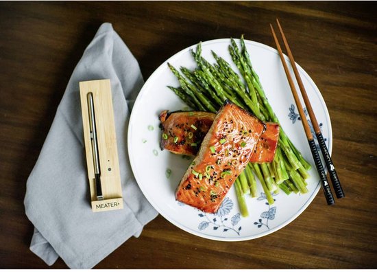 Twee stukken zalmfilet met asperges op een bord, met een Meater+ thermometer in houten houder en eetstokjes.
