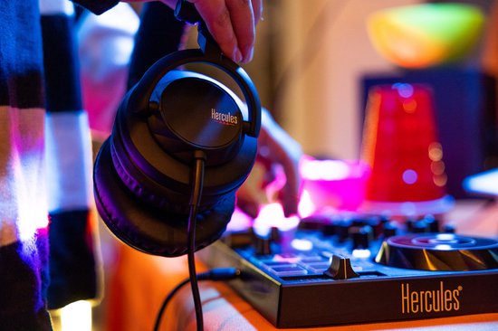 Persoon die een zwarte Hercules DJ-koptelefoon vasthoudt boven een DJ-controller.