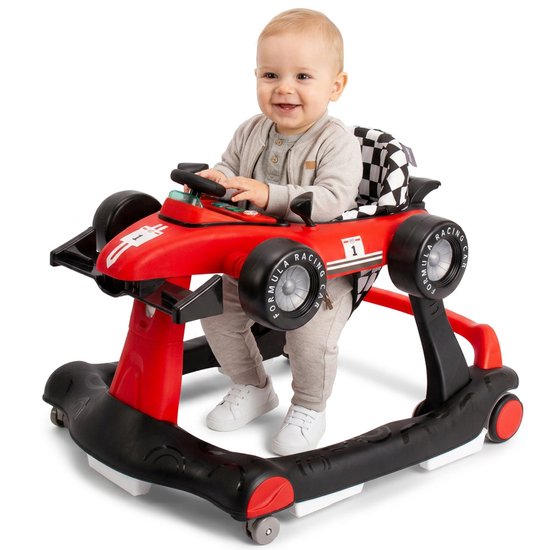 Baby in een rode racewagen loopstoel, zittend met de handen op het stuur.