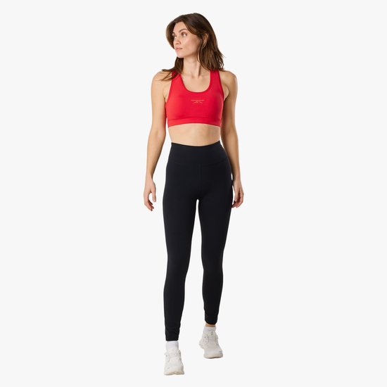 Model draagt een rode sportbeha en zwarte legging. Ze kijkt naar links.