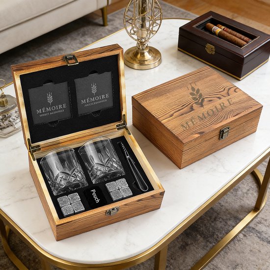 Houten kist met whiskeyglazen, stenen en tang, naast een sigarendoos op een marmeren tafel.