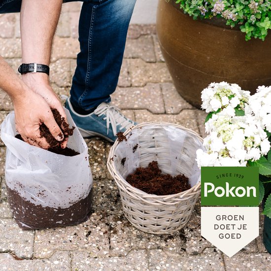 Handen met donkere potgrond boven een gevlochten mandje met potgrond.