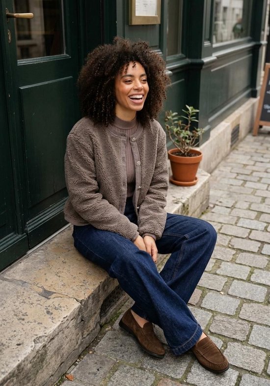 Model draagt een taupe teddy bomberjack over een taupe coltrui en donkerblauwe jeans.