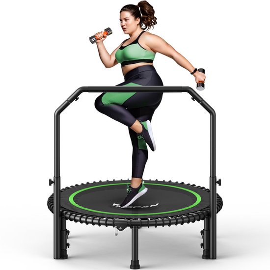 Vrouw met groene accenten op de outfit, springend op zwarte trampoline met groene rand, met dumbbells.