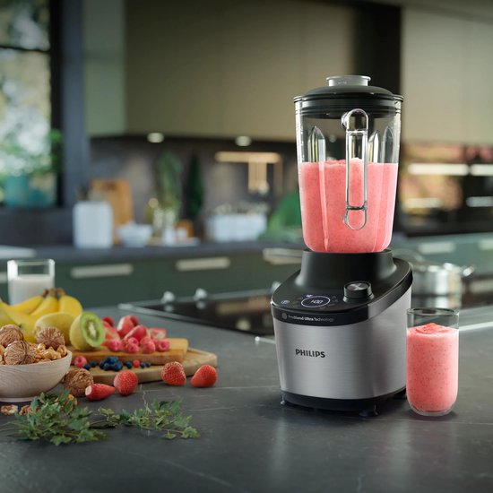 Philips blender met fruitmengsel in de kan en een glas smoothie ernaast.