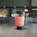 Blenderkan met een roze smoothie op een aanrecht.