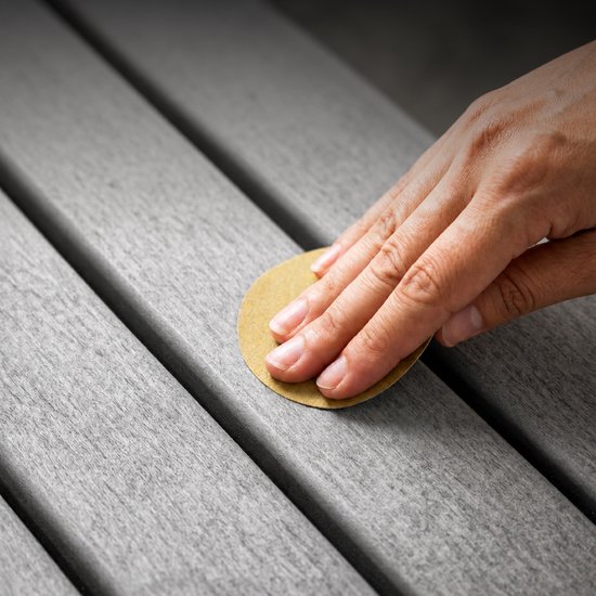 Hand met schuurpapier schuurt een grijze ribbelmat.