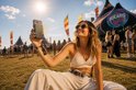 Vrouw met zonnebril, zittend in het gras, laadt haar telefoon op met een magnetische zonnepaneel powerbank.