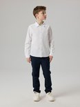 Jongen draagt wit katoenen overhemd met geborduurd logo en donkere broek.