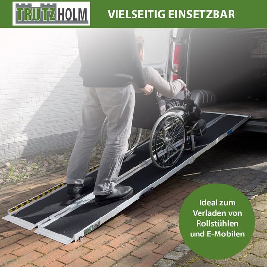 Een persoon duwt een rolstoel over een aluminium oprit met zwart antislipoppervlak, bij een busje.