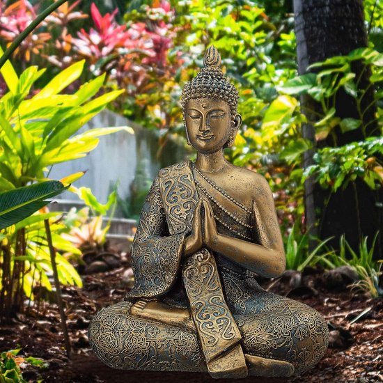Gouden boeddhabeeld in meditatiehouding, zittend te midden van weelderige groene planten in een tuin.