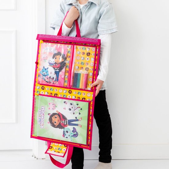 Kind met lichte spijkerjas draagt een draagtas met Gabby's Poppenhuis tekenspullen. De tas bevat kleurboeken en potloden.
