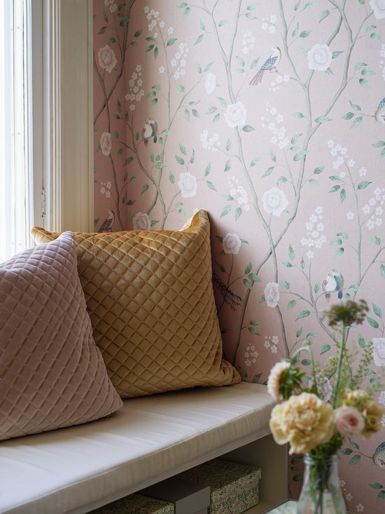 Roze bloemenbehang met vogels, in een kamer met een vensterbank en kussens.