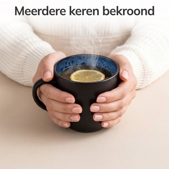 Handen houden een zwarte mok met blauw gespikkeld interieur, gevuld met thee en een citroenschijfje.