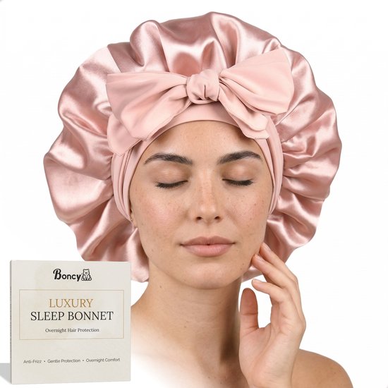 Vrouw met gesloten ogen draagt een roze satijnen slaapmuts met strik. Naast haar de doos 'Boncy LUXURY SLEEP BONNET'.