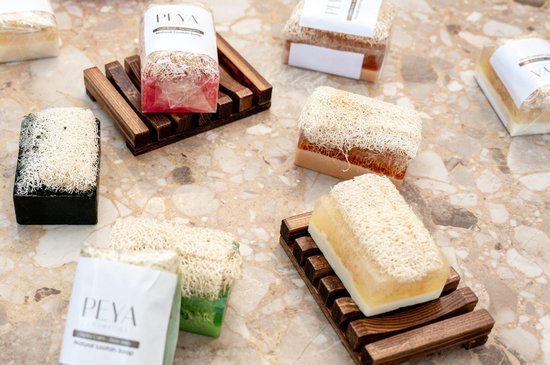 Zes stukken natuurlijke loofah zeep met houten zeepbakjes op een marmeren achtergrond.