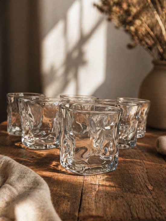 Ensemble de six verres transparents à la surface irrégulière et ondulée, posés sur une table en bois.