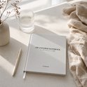 Crème gekleurd zwangerschapsdagboek van Planbooks op een lichtgekleurde tafel, naast een glas water en een pen.