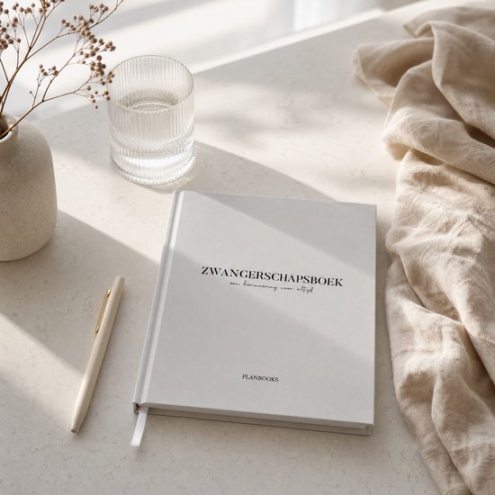 Crème gekleurd zwangerschapsdagboek van Planbooks op een lichtgekleurde tafel, naast een glas water en een pen.