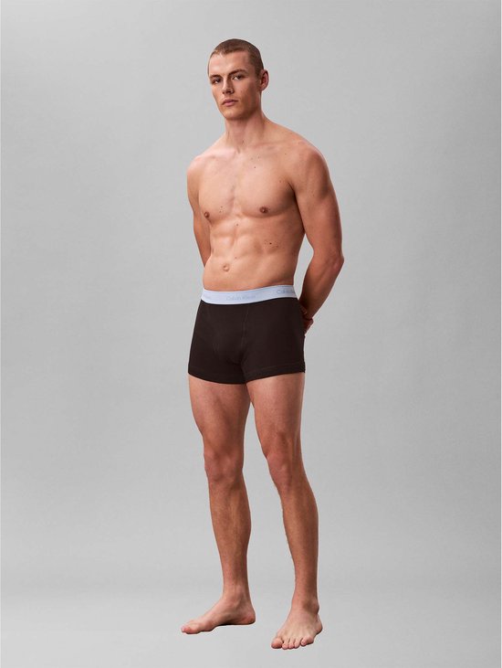 Man met bruine boxershorts met grijze Calvin Klein band, handen achter de rug.