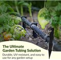 Zwarte grondpennen in een tuinbed met tomatenplanten en een druppelslang, met tekst "The Ultimate Garden Tubing Solution".