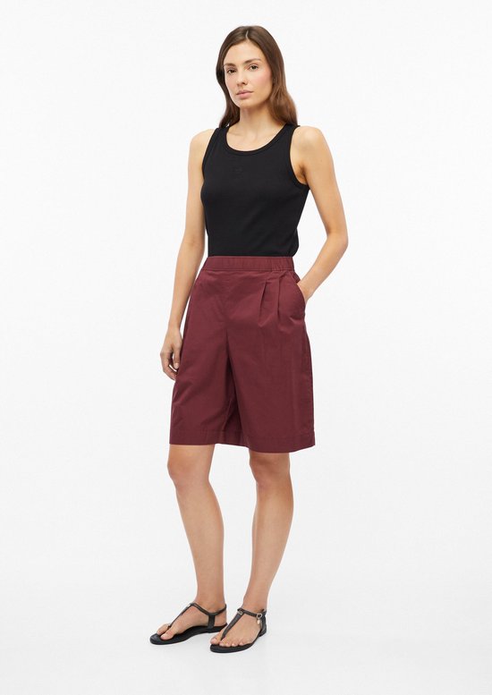 Een model draagt een zwarte tanktop en wijnrode shorts met elastische tailleband, wijde pijpen en insteekzakken.