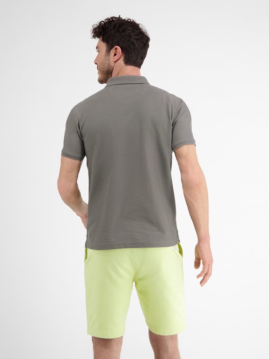 Man in donkergrijs poloshirt en lichtgroene korte broek, zicht van achteren.