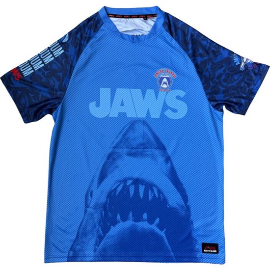 Maillot bleu Jaws avec imprimé de gueule de requin sur le devant, texte 'JAWS' et logo 'AMITY ISLAND SWIM CLUB'.