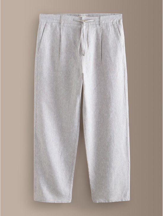 Beige linnen broek met plooien en wijde pijpen op een neutrale achtergrond.