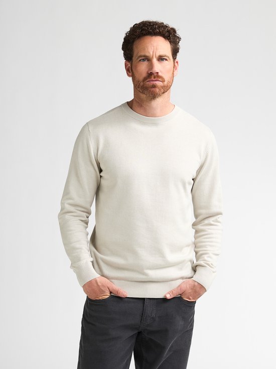 Man met beige trui met lange mouwen en handen in de zakken.